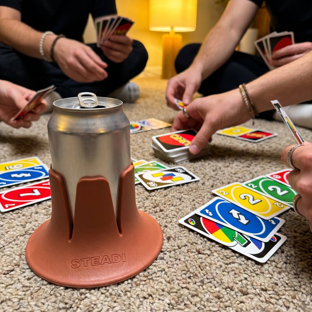 A can standing in a terracotta Steadi on a low carpeted floor beside a lamp and a game.